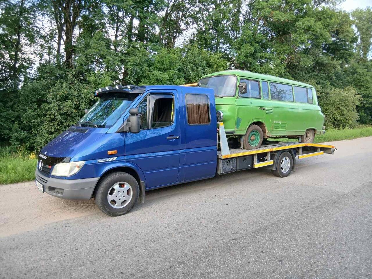 Синій евакуатор перевозить зелений автобус